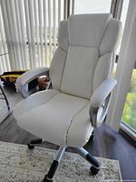Front view showing white faux leather upholstery, padded armrests, roller caster base, and ergonomic design.
