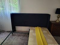 Side view of the king size dark royal blue winged headboard mounted and partially accompanied by one mattress section showing the frame and wheels.