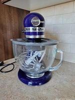 Front view of cobalt blue stand mixer with glass bowl and flat beater in place.