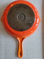 Bottom view of Le Creuset frying pan showing orange enamel coating and cast iron base with embossed logo and size 25