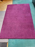 Rectangular grape-colored carpet laid on floor showing fluffy texture and color.