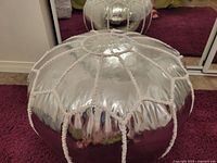 Front angle showing round metallic silver pouf with rope trim and stuffed cushion.