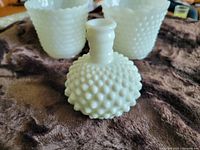Photo showing the three white milk glass hobnail pattern items: two plant pots and one small vase on a brown surface.
