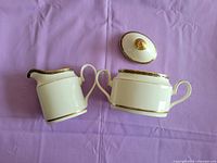 Top view of the cream pitcher and sugar bowl with lid, showing gold detailing on rims and handles, lying on a purple fabric background.