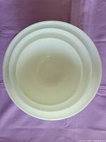 Top down view showing all three nested white milk glass bowls arranged inside one another on purple fabric background.