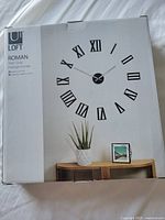 Box showing complete product with Umbra Loft branding and Roman numeral clock displayed on wall above furniture.
