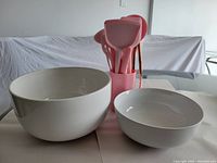 Photo showing the two white bowls and the pink kitchen utensil set in holder, against a neutral background.