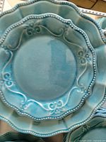 Close-up photo showing the teal plates with decorative beaded and floral scroll rim design.