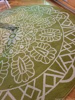Close-up of round carpet showing green base with white ornate floral and geometric design.