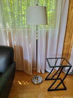Standing floor lamp next to black leather couch and glass top side tables, showing lamp height and overall style