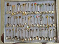 Photo showing 48 souvenir spoons arranged in rows within a frame, each with colorful and intricate designs on the handles representing various countries and landmarks.