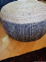 Side angle of the straw pouf ottoman showing the woven black and natural straw material.