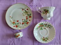 Photo showing all items: plate with strawberry pattern, cup and saucer, and napkin ring on lavender cloth