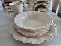 Photo showing stacked cream-coloured bowls, side plates, and dinner plates with bead-edge detail and subtle floral embossing