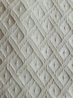 Close-up of the fabric's textured diamond and dot geometric pattern in light moss green color.