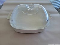 Full view of white Corning Ware microwave browning dish with clear glass lid on top, showing shape and size.