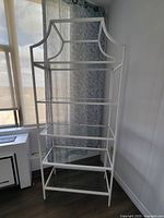 Front view of the white metal display unit showing five glass shelves and decorative top frame.