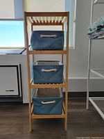 Front view of wooden shelving unit with three teal fabric baskets stacked vertically.