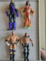 Four wrestling action figures: The Undertaker, Shawn Michaels, Triple H, The Ultimate Warrior, roughly 7 inches tall, placed out flat on a surface.
