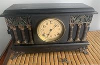 Front view of antique Baldwin mantel clock showing ornate black wooden case with columns and brass detail, round clock face with black Arabic numerals and black hands.