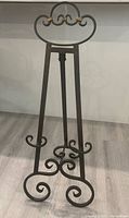 Front view of black iron easel showing scroll design and brass accent bands.