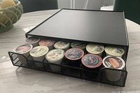 Black metal coffee pod storage drawer with sliding tray partially pulled out showing 12 K-Cup pods in one row visible.