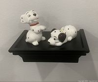 Two 101 Dalmatians Disney figurines, 'Go Get Him Thunder' sitting and 'Lucky' lying down, displayed on a black shelf