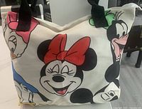 Front and side view of Disney canvas tote bag featuring Minnie Mouse, Goofy, Donald Duck, and Daisy Duck with black shoulder straps.