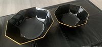 Two octagonal black bowls with gold rims shown side by side on a black surface. The 9 inch is larger and placed behind the smaller 7 inch bowl.