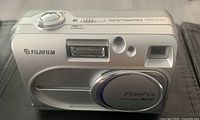 Front view of the silver Fujifilm FinePix A210 camera with lens cover closed, visible flash and viewfinder.