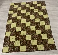 Full view of the handmade quilt laid flat on the floor showing the patchwork olive-green and floral brown squares.