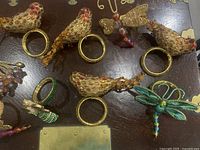 Top view of nine decorative napkin rings featuring bird, dragonfly, and butterfly designs with metal and bead details on a dark wooden surface.