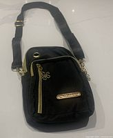 Front view of black cross body bag with gold-tone zipper pulls and brand plaque.