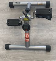 Top-down view of the InStride folding seatless exercise cycle showing pedal straps, central tension control knob, electronic monitor, rubber feet and metal frame.