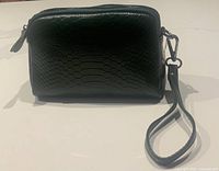 Front view of green leather snake pattern cross body bag with wrist strap lying beside