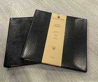 Two new black Gallery Leather scrapbooks displayed on light wood floor, front view with label.