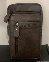 Front view of new brown top-grain leather waist pack showing zippered compartments and embossed branding on leather.