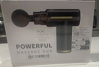 Front view of the sealed box showing a black handheld massage gun with a rounded massage head and label 'POWERFUL MASSAGE GUN'.