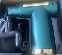 Green metallic massage gun with gold accent alongside four different shaped black massage heads: round, forked, flat, and bullet-shaped.