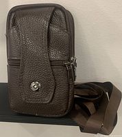 Front view of the genuine brown leather phone waist bag with visible snap button on front flap pocket and adjustable strap coiled beside.