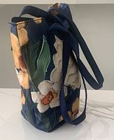 Side view showing the bucket shape and floral print on navy fabric with shoulder strap.