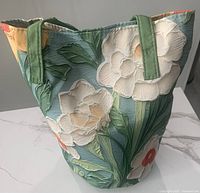 Front view of floral bucket bag showing textured three-dimensional floral pattern and green straps