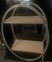 Front corner view showing two-tier shelf with oval silver metal frame and wood shelves.