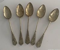Five silver demitasse spoons laid side by side showing the ornate handle designs and spoon bowls.