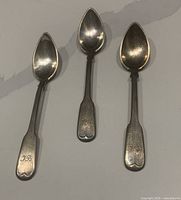 Top view of the three silver spoons showing the tear-drop shaped bowls and engraved initials on long slender handles.