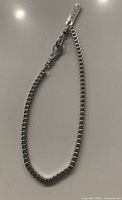 Sterling silver box chain bracelet shown closed with cross detail near clasp, on flat surface.