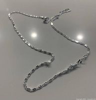 Close-up image of the silver chain showing twisted link design and lobster clasp closure.