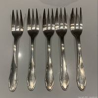 Five sterling silver cocktail forks arranged side by side showing front design with handles featuring decorative pattern