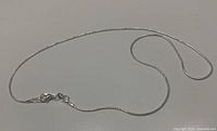 Full view of the thin sterling silver snake chain necklace with lobster clasp laid flat showing entire length and clasp detail.