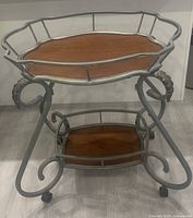 Mid-century vintage two-tier bar cart side view showing metal frame and wood shelves on caster wheels.